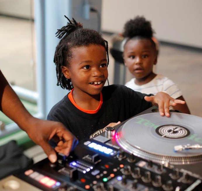 Two young children touching a DJ's equipment. 